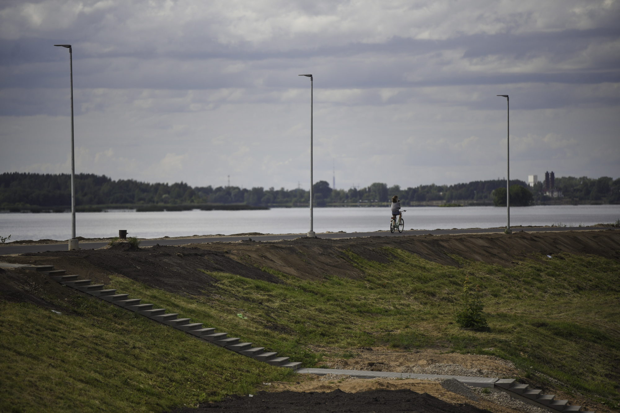 Atjaunotais Ik&scaron;ķiles aizsargdambis, meitene minas ar velosipēdu gar asfaltēto Daugavas upes krasta ceļu