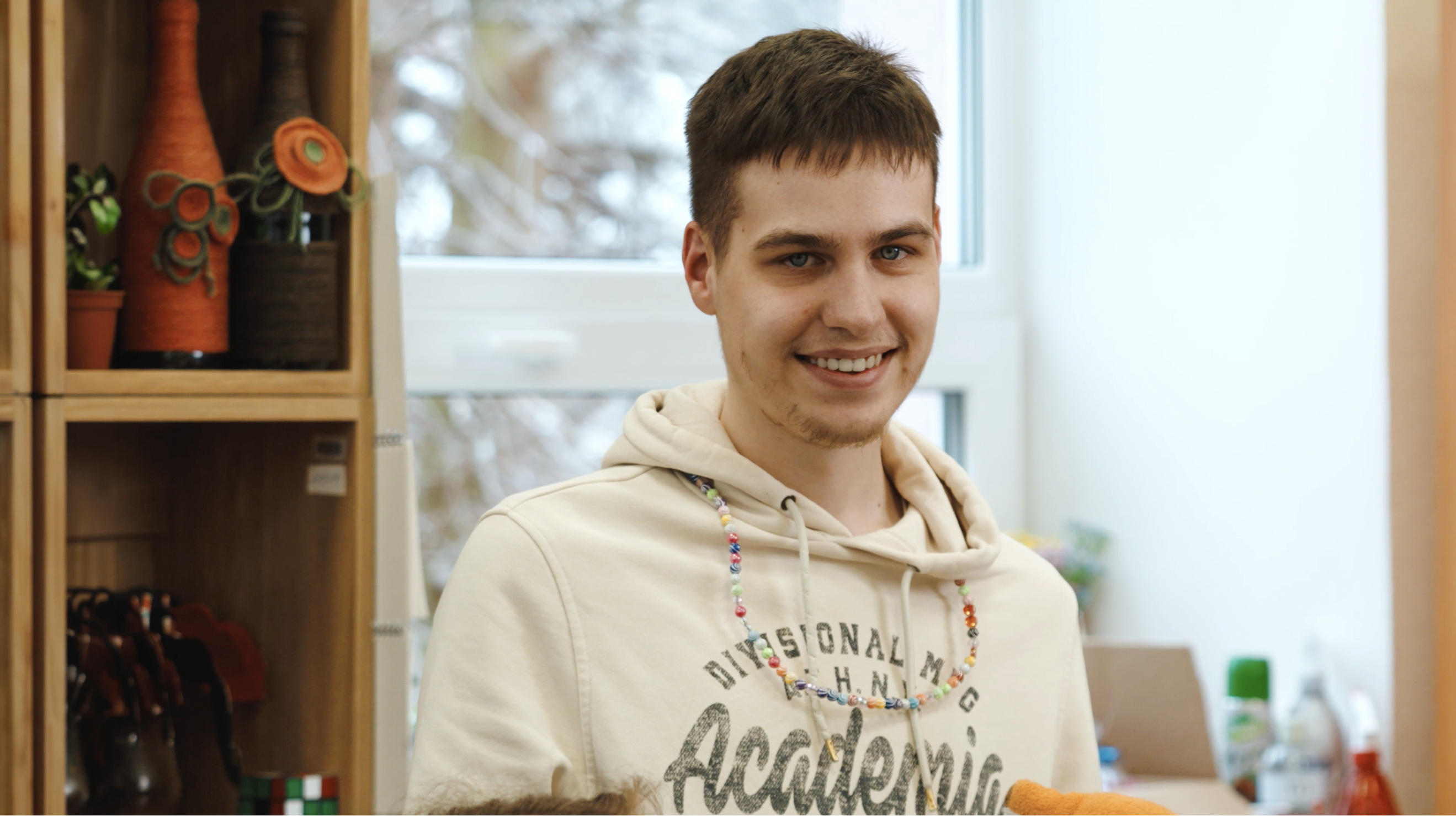 Foto portrets &ndash; smaidīgs jaunietis ar īsiem, brūniem matiem un baltā hūdijā