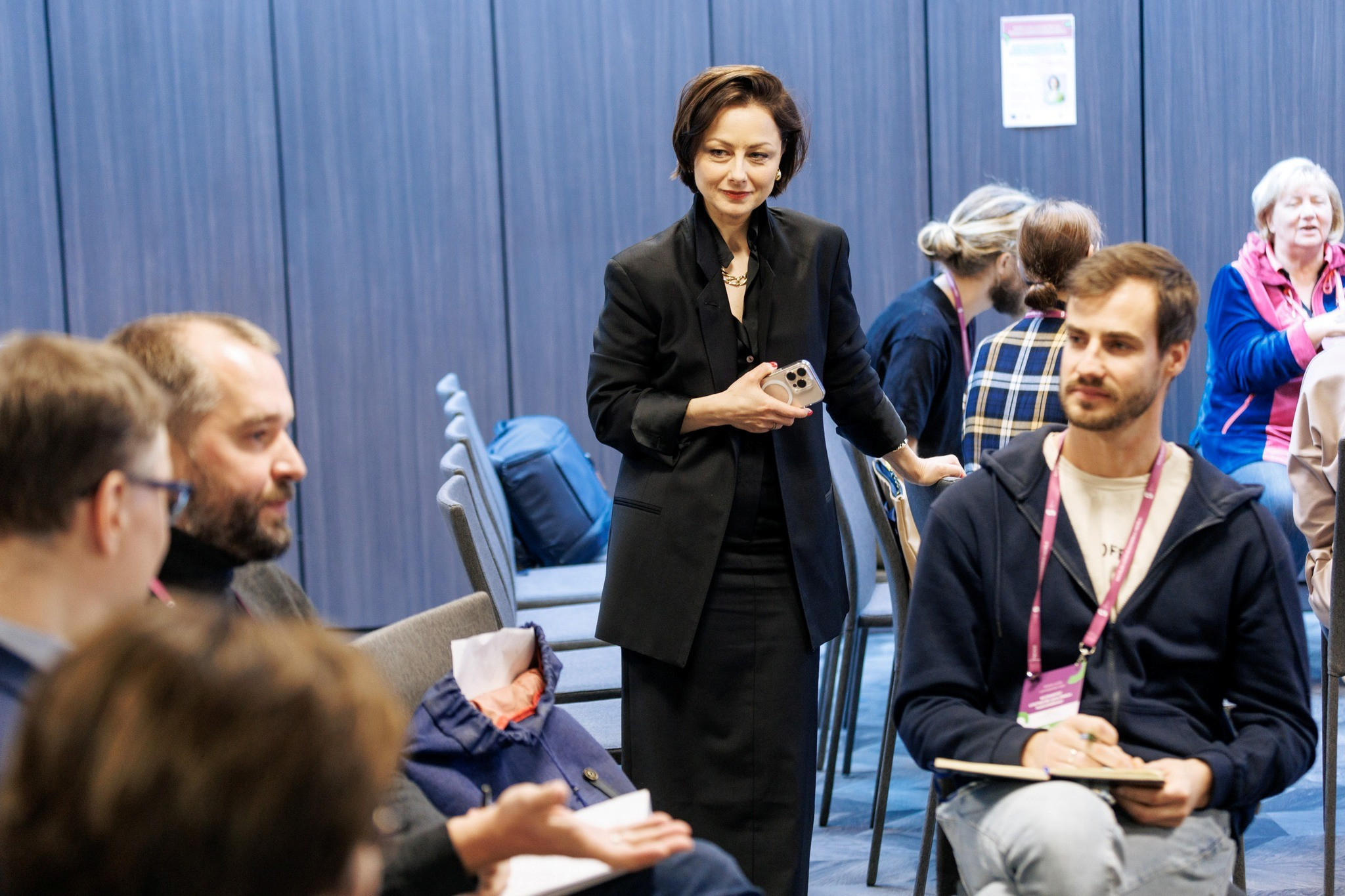 Olga Kazāka, pasākuma vadītāja, stāv un vēro kā cilvēki darba grupās strādā