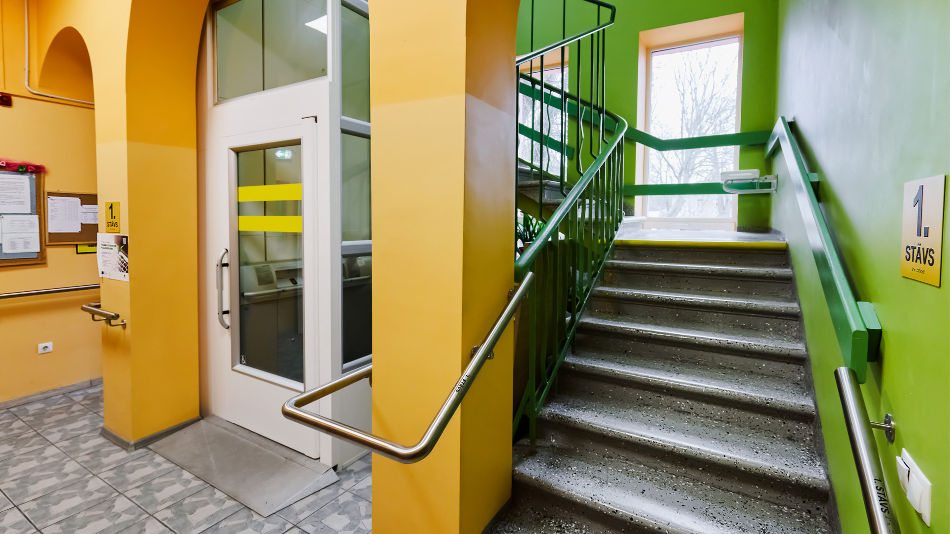 Kāpņu telpa. Sienas krāsotas zaļā un dzeltenā krāsā, tumši pelēka flīzēta grīda, tumši pelēkas kāpnes. Margas apbās trepju pusēs. Lifta durvis kreisajā pusē.