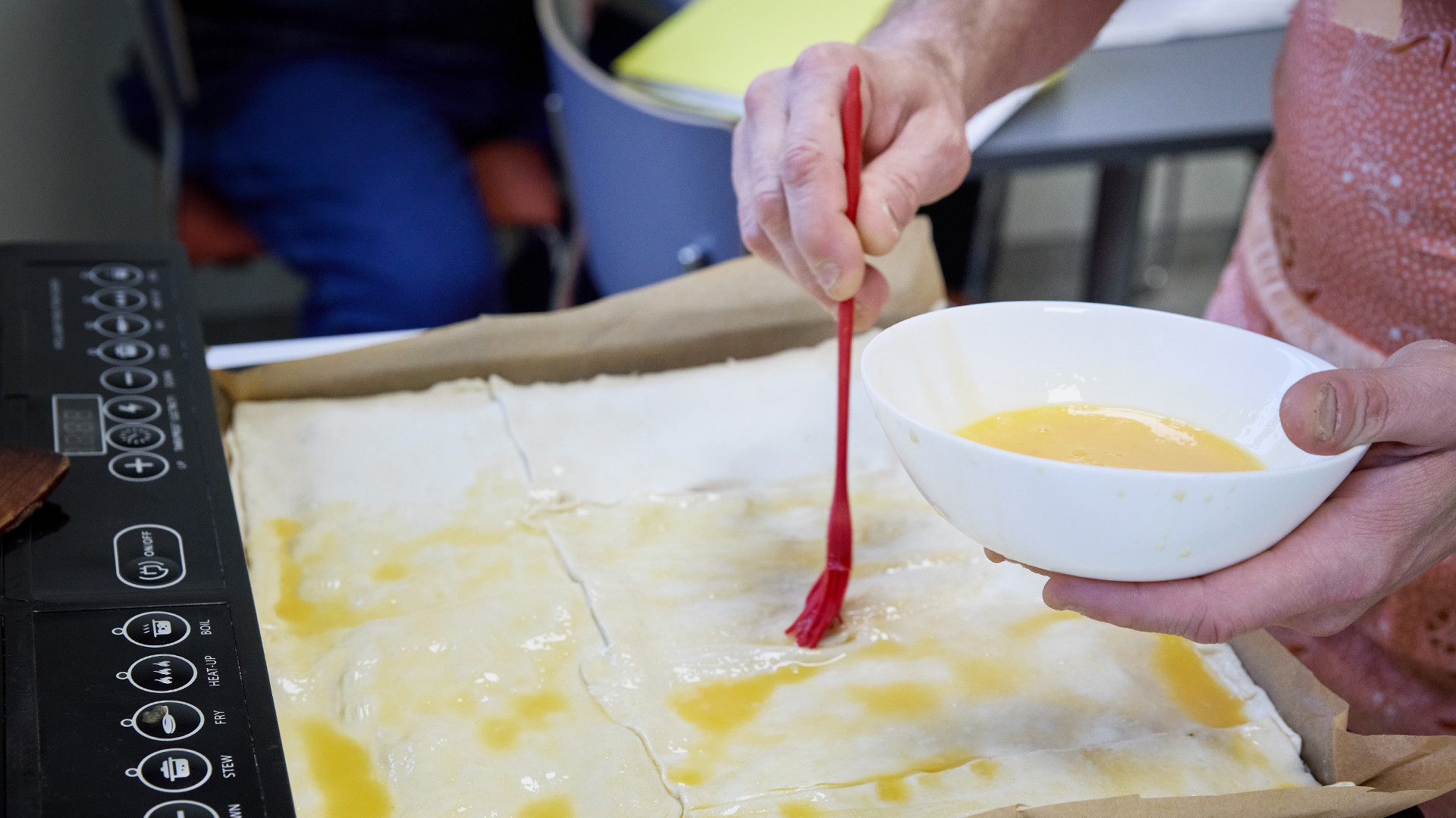 Uz pannas izrullēta mīkla. Sieviete to ieziež ar olas dzeltenumu