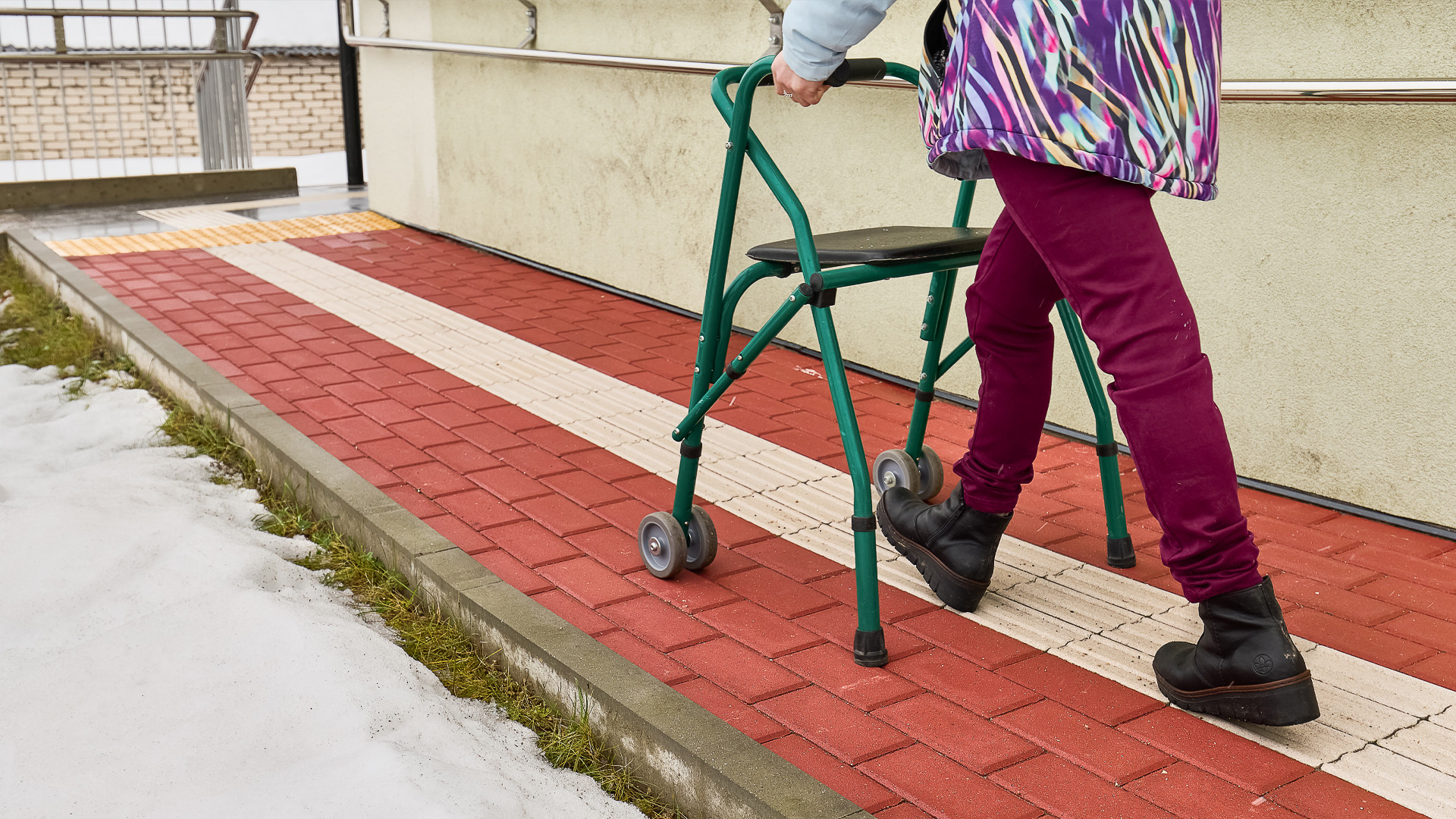 Sieviete ar staigulīti iet pa sarkanu bruģētu celiņu
