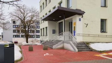 Ēkas ārpuse. Pilsēta, sarkans bruģis, māja ar gaiši saļu, jaunu fasādi, kāpnes ar hormētām margām