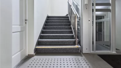 Kāpņu telpa. Vienā pusē kāpnes, otrā lifts.