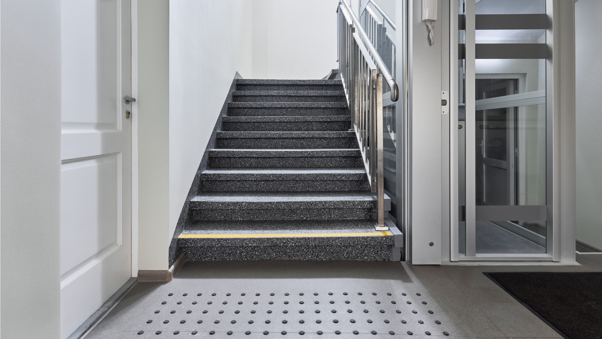 Kāpņu telpa. Vienā pusē kāpnes, otrā lifts.
