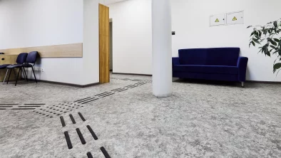 Vestibils ar stabu pa vidu. Pie sienas zils dīvāns. Uz grīdas taktilās joslas