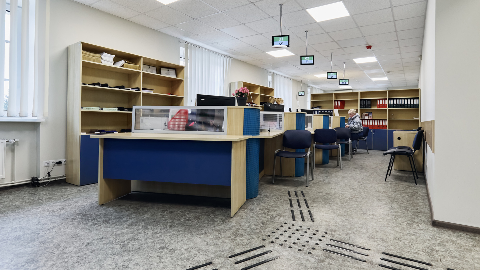 Klientu pieņemšanas telpa ar vairākiem galdiem un krēsliem
