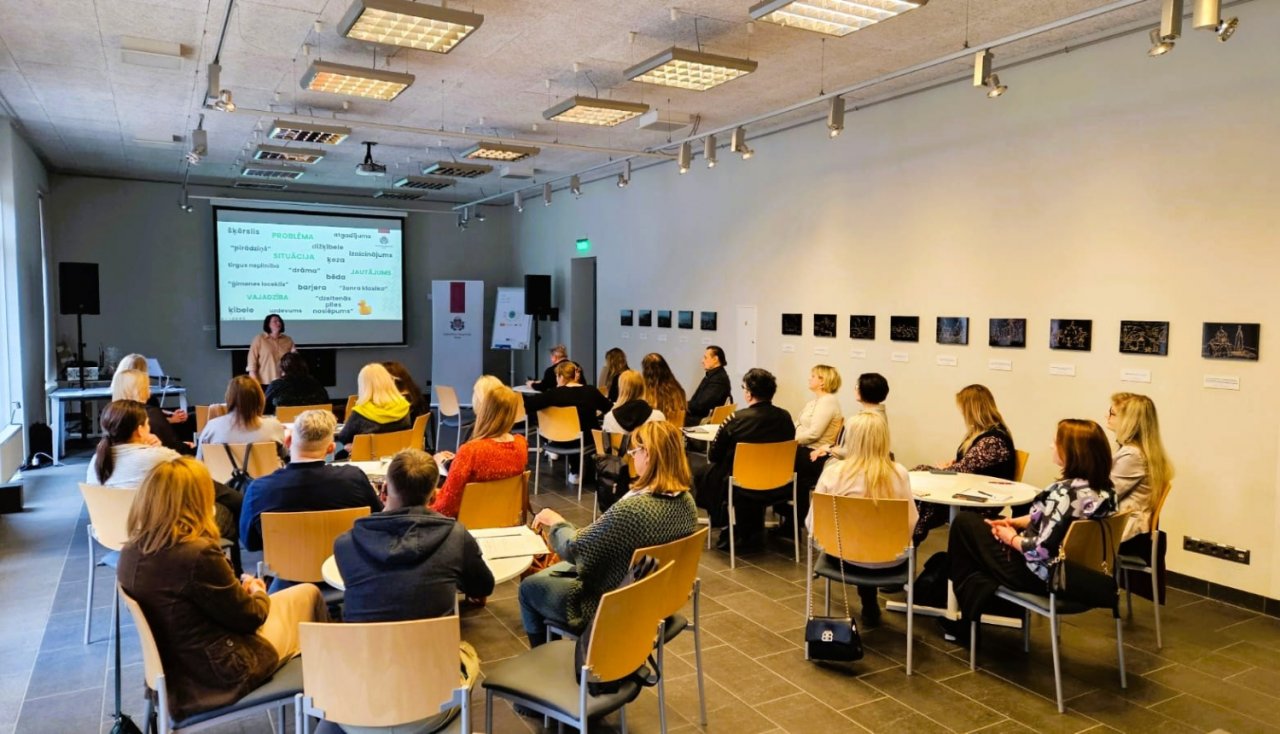 neliela konferenču telpa. Pie ekrāna stāv lektore un aptuveni 50 cilvēkiem kaut ko stāsta