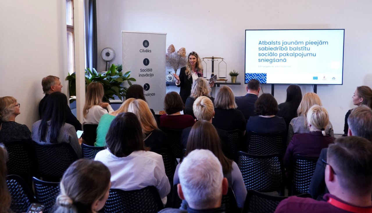 Lekciju telpa ar cilvēkiem auditorijā un lektori pie ekrāna