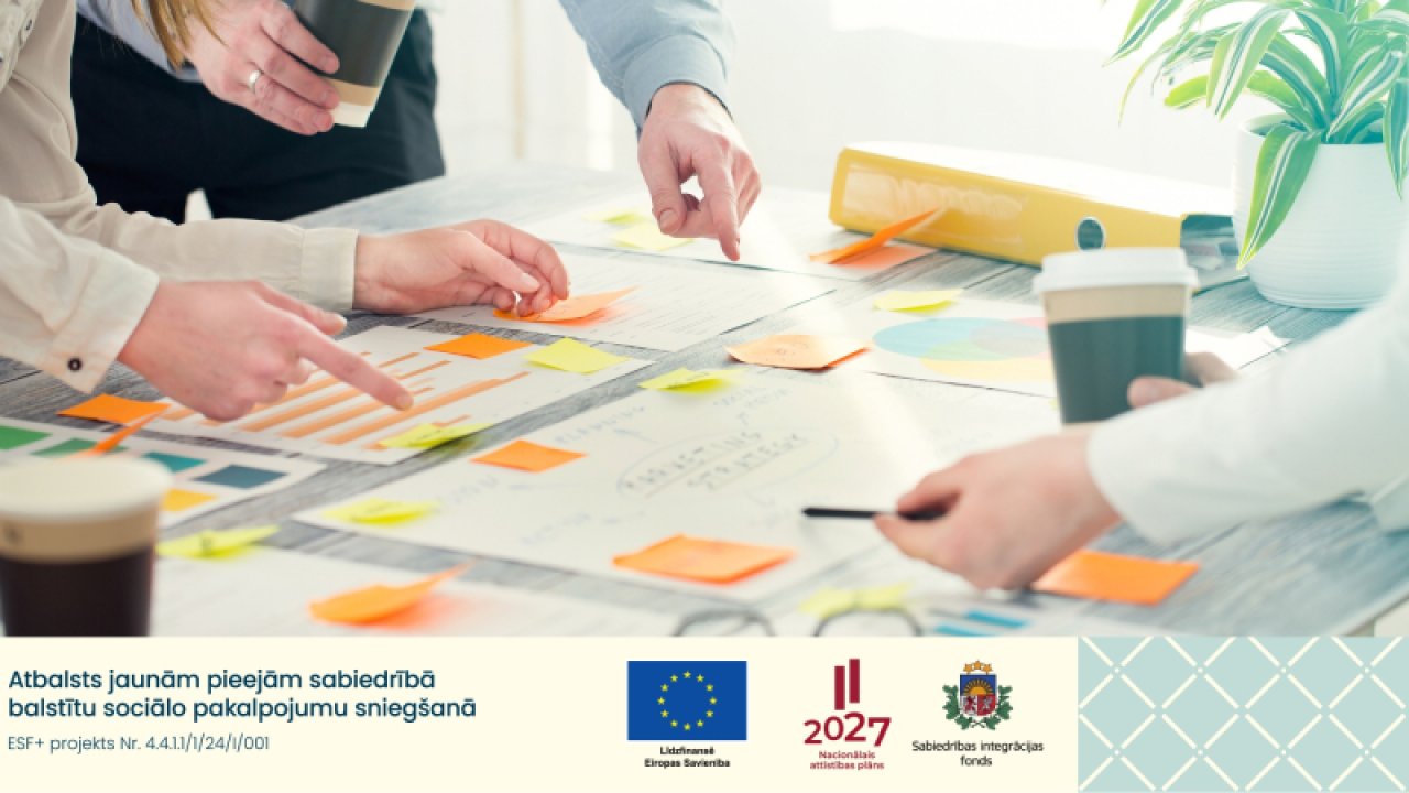 biroja darba galds. Uz tā trīs cilvēki līmē līmlapiņas, šadi veidojot stratēģiju