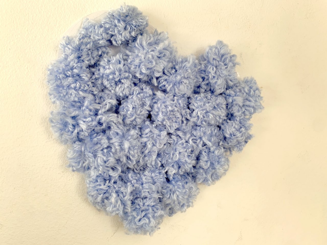 No zilas dzijas veidota sirds uz bēšīgas sienas