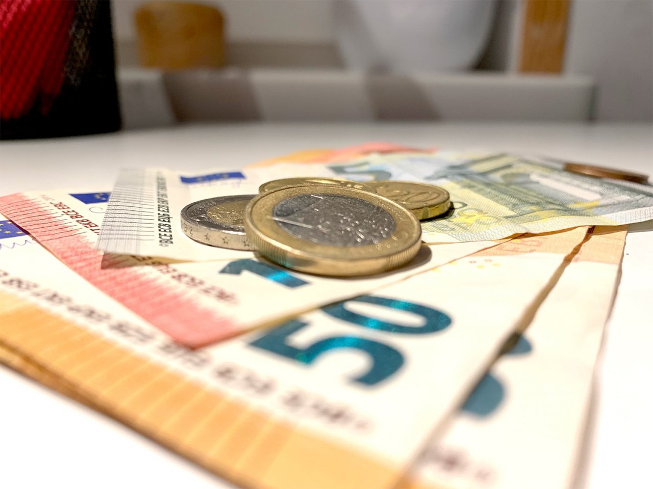 Uz balta galda noliktas vairākas eiro banknotes un monētas