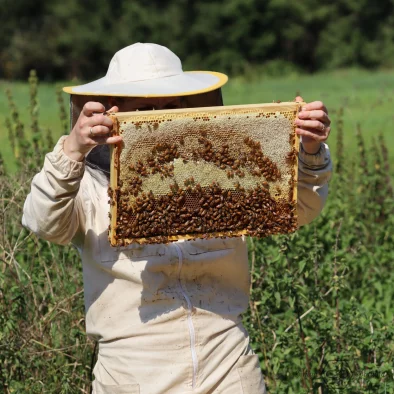 Dravinieks baltā apģērbā tur rokās medus kāri
