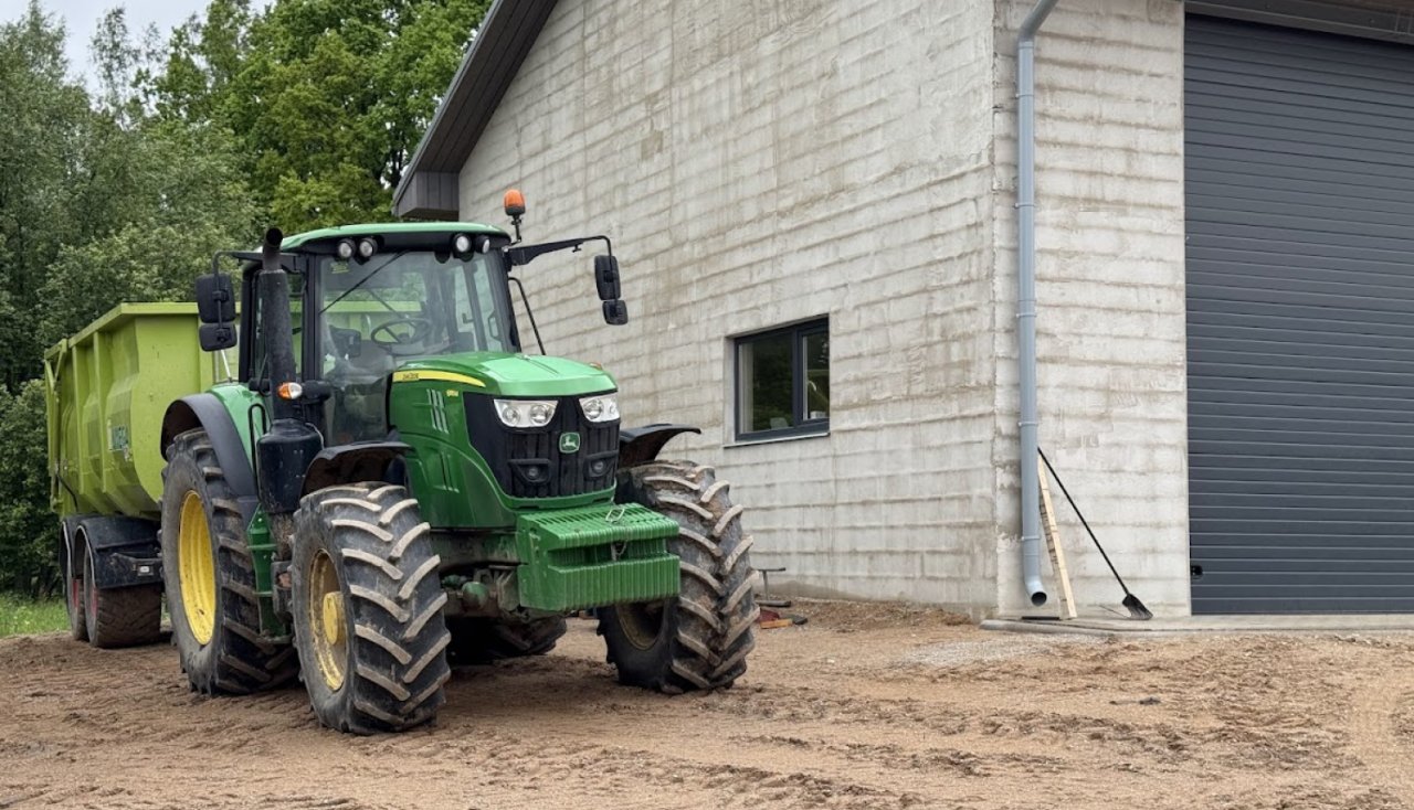zaļš traktors stāv pie saimniecības ēkas stūra