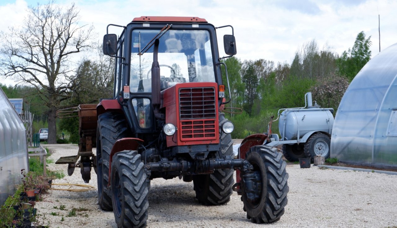 sarkans traktors stāv starp siltumnīcām